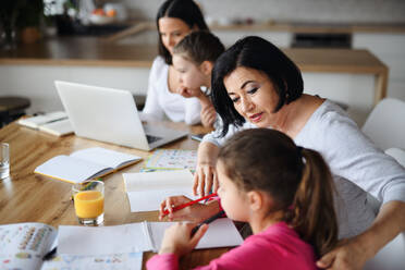 Glückliche kleine Schwestern mit Mutter und Großmutter machen Hausaufgaben mit Laptop drinnen zu Hause, Home-Office und Homeschool-Konzept. - HPIF07521