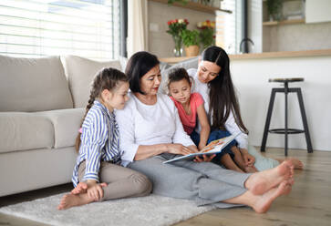 Portrait of happy small girls with mother and grandmother indoors at home, reading story book. - HPIF07525