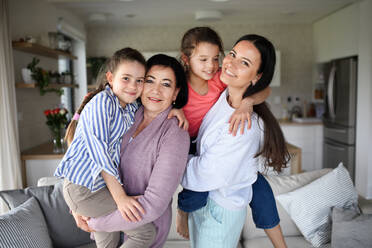 Portrait of happy small girls with mother and grandmother indoors at home, looking at camera. - HPIF07531