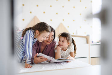 Glückliche kleine Mädchen mit einer älteren Großmutter drinnen im Schlafzimmer zu Hause, auf dem Bett lesend - HPIF07535