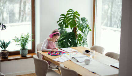 School girl with headphones sitting and working at table indoors at home, distance learning. - HPIF07545