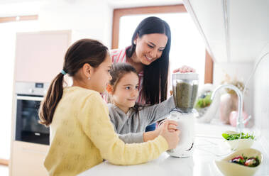 Mother with girls indoors at home, preparing healthy fruit smoothie drink. - HPIF07548