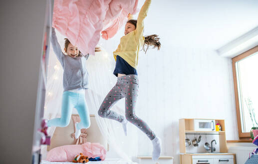 Zwei fröhliche kleine Mädchen Schwestern drinnen zu Hause, springen auf dem Bett im Schlafzimmer. - HPIF07549