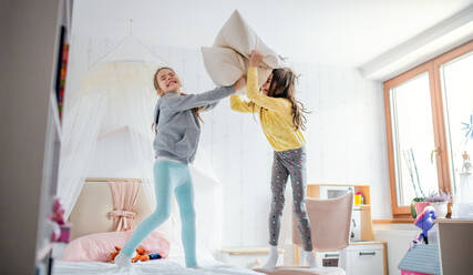 Two cheerful small girls sisters indoors at home, pillow fight on bed in bedroom. - HPIF07553