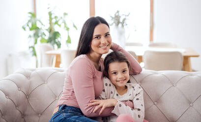Porträt einer Mutter mit ihrer kleinen Tochter, die zu Hause auf dem Sofa sitzt und in die Kamera schaut. - HPIF07555