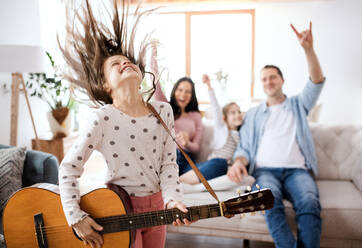 Porträt eines kleinen Mädchens mit Familie zu Hause, das sich mit einer Gitarre vergnügt. - HPIF07558