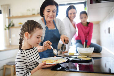 Glückliche kleine Mädchen mit Mutter und Großmutter, die zu Hause Pfannkuchen backen und kochen. - HPIF07564