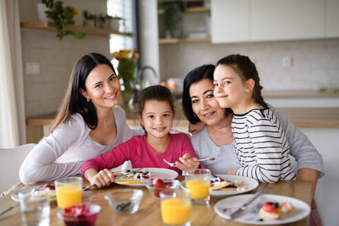 Glückliche kleine Mädchen mit Mutter und Großmutter, die zu Hause Pfannkuchen essen und in die Kamera schauen. - HPIF07565