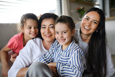 Happy small girls with a mother and grandmother indoors at home, sitting on floor and looking at camera - HPIF07569