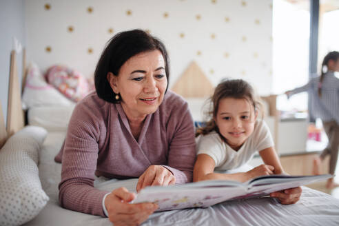 Ein glückliches kleines Mädchen mit einer älteren Großmutter im Schlafzimmer zu Hause, die auf dem Bett liest. - HPIF07577
