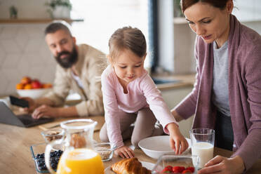 Eine Familie mit kleiner Tochter drinnen in der Küche, Alltag und Home Office mit Kinderkonzept. - HPIF07580