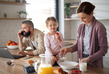 Eine Familie mit kleiner Tochter drinnen in der Küche, Alltag und Home Office mit Kinderkonzept. - HPIF07581