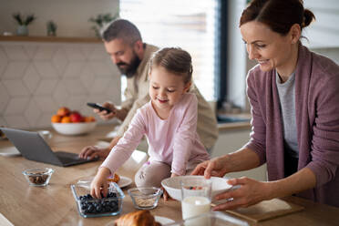 Eine Familie mit kleiner Tochter drinnen in der Küche, Alltag und Home Office mit Kinderkonzept. - HPIF07582