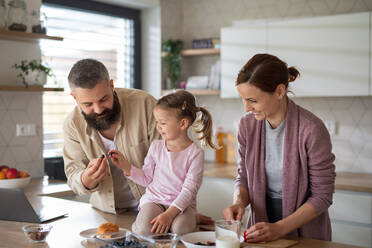Eine Familie mit kleiner Tochter drinnen in der Küche, Alltag und Home Office mit Kinderkonzept. - HPIF07584