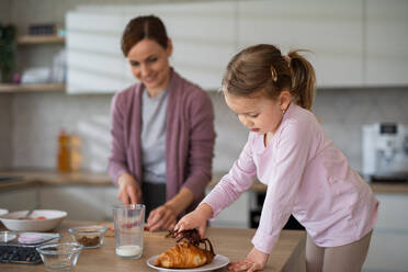 Glückliche Mutter mit kleiner Tochter drinnen in der Küche zu Hause bei der Vorbereitung des Frühstücks, Alltagskonzept. - HPIF07589
