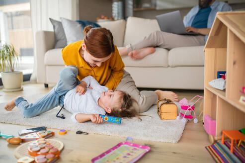 Eine Mutter mit kleiner Tochter spielt drinnen zu Hause, Alltag und Home Office mit Kind Konzept. - HPIF07608