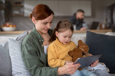 Eine glückliche Mutter mit ihrer kleinen Tochter, die sich zu Hause ein Kinderprogramm auf einem Tablet ansieht, ein Konzept für Alleinerziehende. - HPIF07616