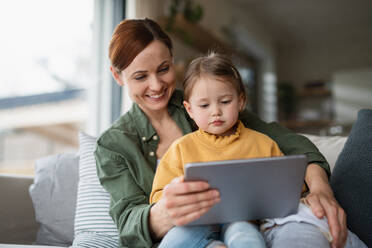 A happy mother with small daughter watching kids programme on tablet indoors at home, single parenting concept. - HPIF07617