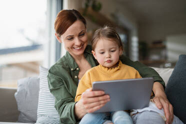 Eine glückliche Mutter mit ihrer kleinen Tochter, die sich zu Hause ein Kinderprogramm auf einem Tablet ansieht, ein Konzept für Alleinerziehende. - HPIF07617