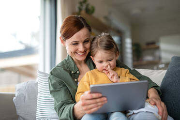 Eine glückliche Mutter mit ihrer kleinen Tochter, die sich zu Hause ein Kinderprogramm auf einem Tablet ansieht, ein Konzept für Alleinerziehende. - HPIF07618