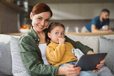 Eine Mutter mit einer kleinen Tochter, die zu Hause ein Tablet benutzt und in die Kamera schaut, Alltag und Home Office mit Kind. - HPIF07619