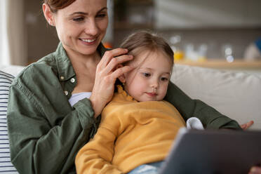 A happy mother with small daughter watching kids programme on tablet indoors at home, single parenting concept. - HPIF07620