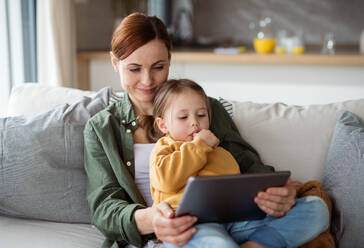 Eine glückliche Mutter mit ihrer kleinen Tochter, die sich zu Hause ein Kinderprogramm auf einem Tablet ansieht, ein Konzept für Alleinerziehende. - HPIF07621