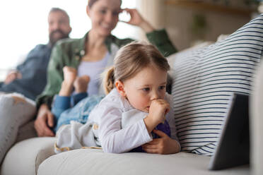 Eine Familie mit einer kleinen Tochter, die zu Hause ein Programm auf einem Tablet ansieht, Konzept des täglichen Lebens. - HPIF07622