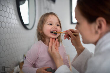 Mother with happy small daughter brushing teeth indoors in bathroom in the evening or morning. - HPIF07625