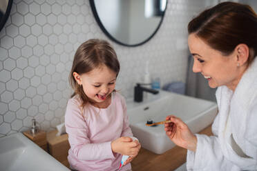 Mother with happy small daughter brushing teeth indoors in bathroom in the evening or morning. - HPIF07626