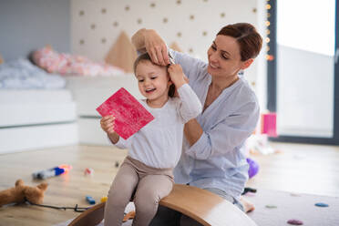 Eine glückliche Mutter mit ihrer kleinen Tochter, die lachend im Schlafzimmer spielt. - HPIF07630