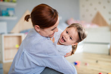 Eine glückliche Mutter mit ihrer kleinen Tochter, die lachend im Schlafzimmer spielt. - HPIF07632