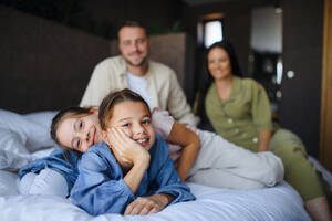 Eine glückliche junge Familie mit zwei Kindern, die in einem Hotel auf dem Bett liegen, Sommerurlaub. - HPIF07648
