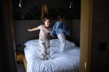 Two little sister jumping on a bed indoors in hotel. - HPIF07650