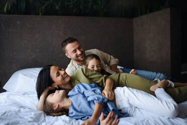 A happy young family with two children lying on bed at hotel, summer holiday. - HPIF07653