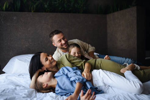 Eine glückliche junge Familie mit zwei Kindern, die in einem Hotel auf dem Bett liegen, Sommerurlaub. - HPIF07653