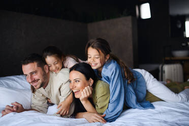 Eine glückliche junge Familie mit zwei Kindern, die in einem Hotel auf dem Bett liegen, Sommerurlaub. - HPIF07655