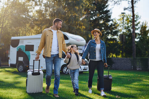 A happy young family walking with suitcases, coming home from caravan trip outdoors in garden - HPIF07656