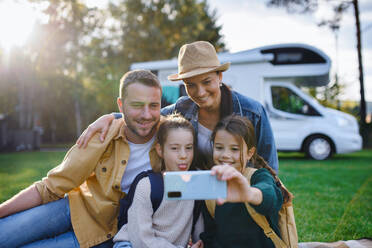 Eine fröhliche vierköpfige Familie hält einen Moment mit ihrem Wohnwagen im Hintergrund fest, während sie ein Selfie im Freien macht - HPIF07666