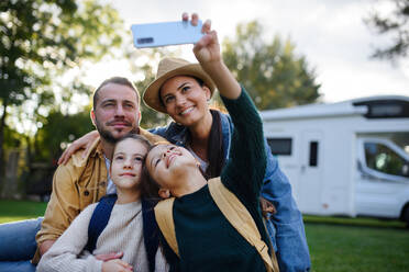 Eine fröhliche vierköpfige Familie hält bei einem Outdoor-Abenteuer einen Moment mit ihrem Wohnwagen im Hintergrund fest - HPIF07669