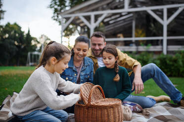 Eine glückliche junge Familie sitzt auf einer Decke und macht ein Picknick zum Mitnehmen im Freien in einem Restaurant. - HPIF07676
