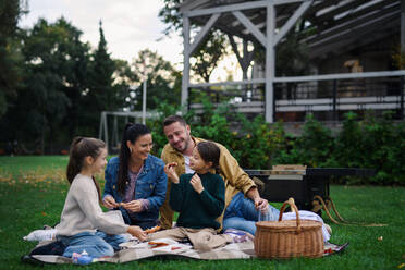 Eine glückliche junge Familie sitzt auf einer Decke und macht ein Picknick zum Mitnehmen im Freien in einem Restaurant. - HPIF07678
