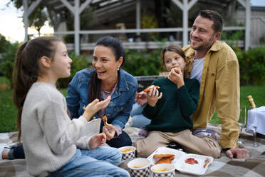 Eine glückliche junge Familie sitzt auf einer Decke und macht ein Picknick zum Mitnehmen im Freien in einem Restaurant. - HPIF07679