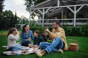 Eine glückliche junge Familie sitzt auf einer Decke und macht ein Picknick zum Mitnehmen im Freien in einem Restaurant. - HPIF07680