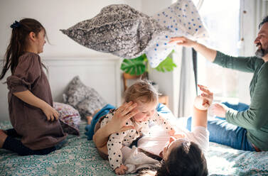 Porträt einer glücklichen Familie mit zwei kleinen Töchtern, die sich zu Hause auf dem Bett vergnügen. - HPIF07699