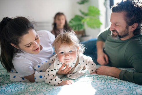 Porträt einer glücklichen Familie mit zwei kleinen Töchtern, die sich zu Hause auf dem Bett vergnügen. - HPIF07700