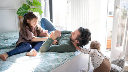 Portrait of happy father with two small daughters having fun on bed at home. - HPIF07702