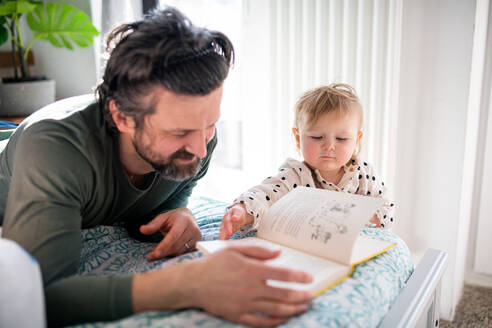 Vater mit glücklicher kleiner Tochter, die zu Hause ein Buch liest. - HPIF07703