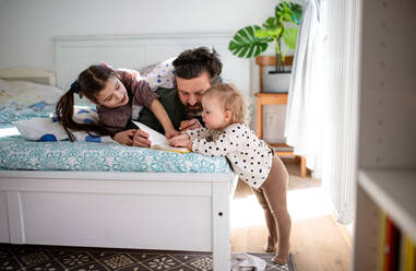 Vater mit zwei glücklichen kleinen Töchtern, die sich zu Hause auf dem Bett vergnügen. - HPIF07704