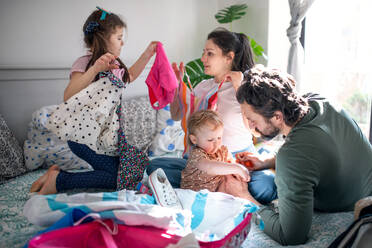 Porträt einer Familie mit zwei kleinen Töchtern beim Packen für den Urlaub auf dem Bett zu Hause. - HPIF07707